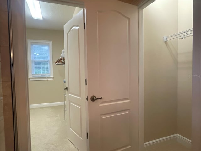 hallway with light carpet, baseboards, and a textured ceiling