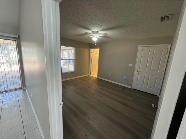 spare room featuring a textured ceiling, wood finished floors, visible vents, a ceiling fan, and baseboards