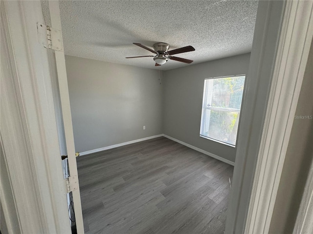 spare room featuring a ceiling fan, a textured ceiling, baseboards, and dark wood-style flooring