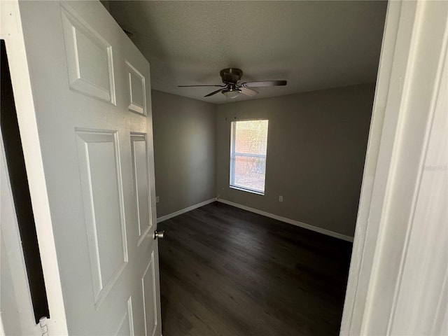 unfurnished room with a textured ceiling, ceiling fan, dark wood-type flooring, and baseboards