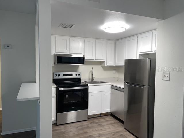 kitchen featuring light wood-type flooring, stainless steel appliances, sink, and white cabinets