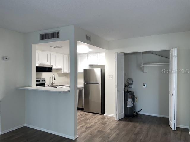 kitchen featuring stainless steel appliances, white cabinetry, electric water heater, and dark hardwood / wood-style floors