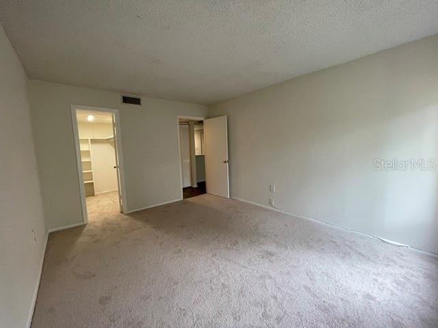 unfurnished bedroom with a walk in closet, light colored carpet, a closet, and a textured ceiling