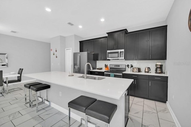 kitchen featuring an island with sink, a breakfast bar area, marble finish floor, stainless steel appliances, and light countertops