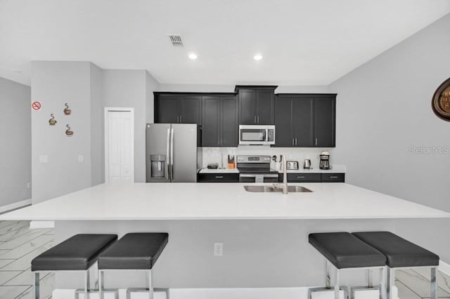 kitchen featuring dark cabinets, a sink, light countertops, appliances with stainless steel finishes, and a large island with sink