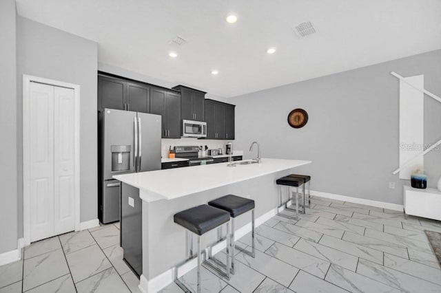 kitchen with marble finish floor, light countertops, appliances with stainless steel finishes, a kitchen island with sink, and a kitchen breakfast bar