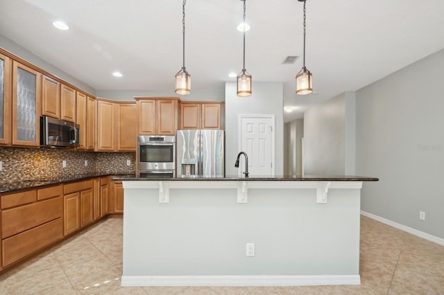 kitchen with pendant lighting, a breakfast bar, appliances with stainless steel finishes, a kitchen island with sink, and tasteful backsplash