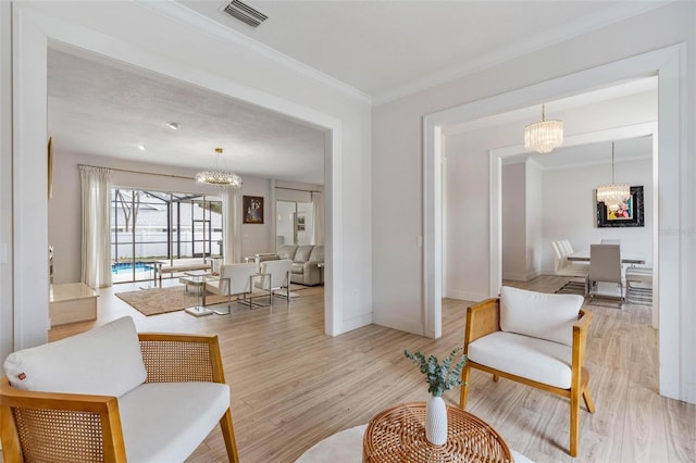 living room featuring crown molding, light hardwood / wood-style flooring, and a notable chandelier