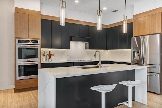 kitchen featuring decorative light fixtures, light stone countertops, an island with sink, and appliances with stainless steel finishes