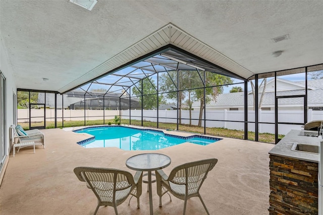 view of pool with an outdoor kitchen, a patio area, and glass enclosure