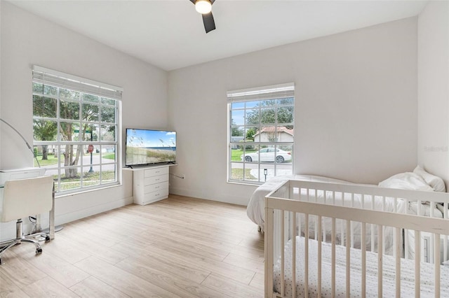 bedroom with ceiling fan, light hardwood / wood-style floors, and a crib