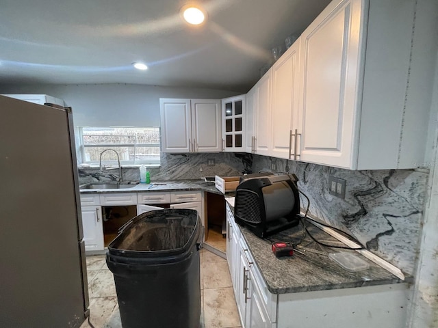 kitchen with sink, white cabinetry, tasteful backsplash, dark stone countertops, and stainless steel refrigerator