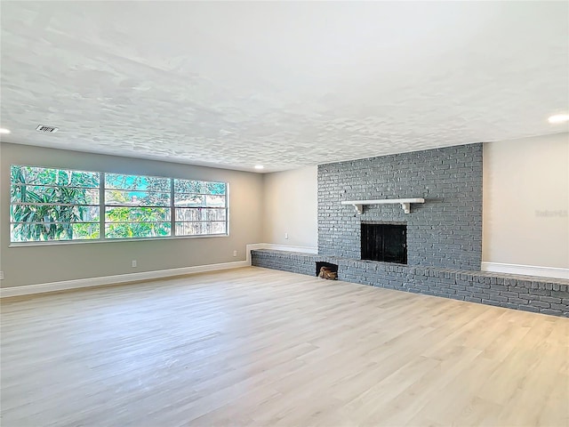 unfurnished living room with light hardwood / wood-style floors, a brick fireplace, and a textured ceiling