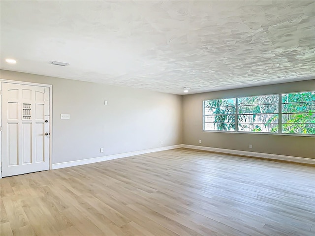 unfurnished room with a textured ceiling and light wood-type flooring