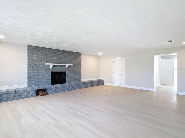 unfurnished living room with a textured ceiling, a brick fireplace, and light wood-type flooring