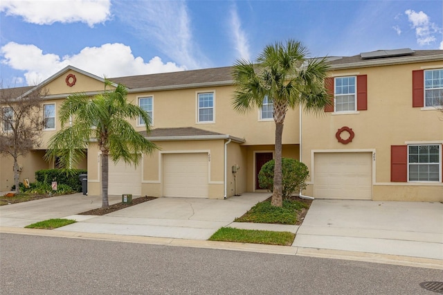 townhome / multi-family property featuring an attached garage, driveway, solar panels, and stucco siding