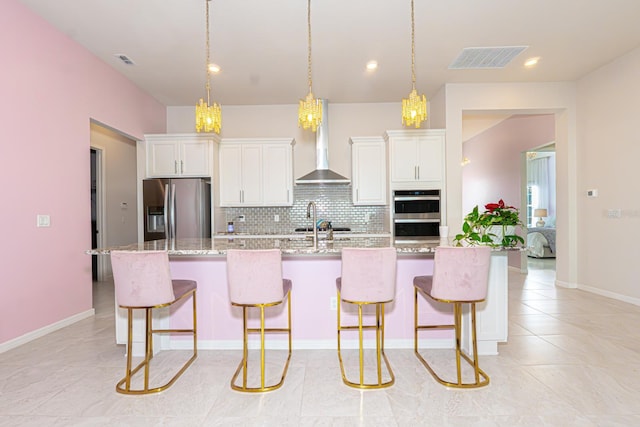 kitchen with wall chimney exhaust hood, appliances with stainless steel finishes, an island with sink, and visible vents