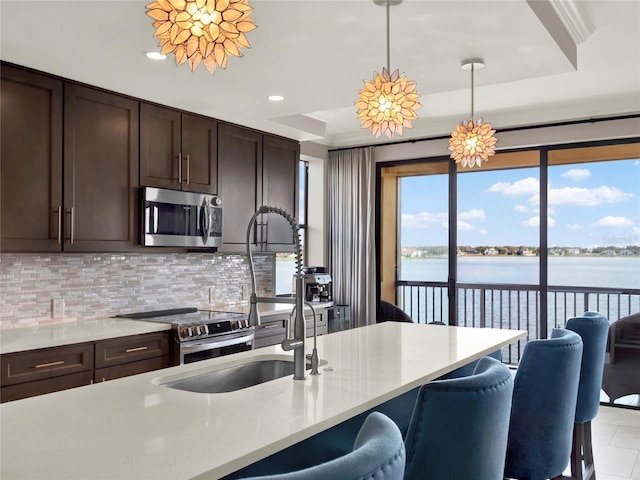 kitchen featuring hanging light fixtures, light countertops, appliances with stainless steel finishes, tasteful backsplash, and a water view