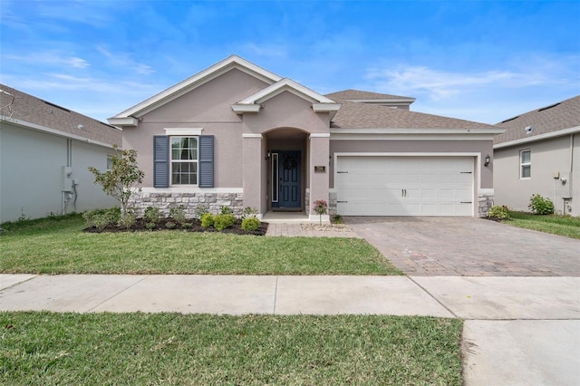 single story home with an attached garage, stone siding, decorative driveway, stucco siding, and a front lawn