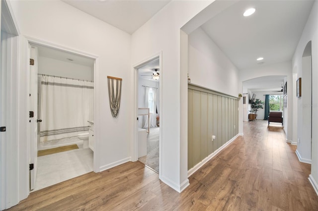 hall featuring baseboards, arched walkways, wood finished floors, and recessed lighting