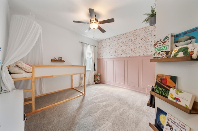 bedroom featuring a wainscoted wall, a ceiling fan, light colored carpet, and wallpapered walls