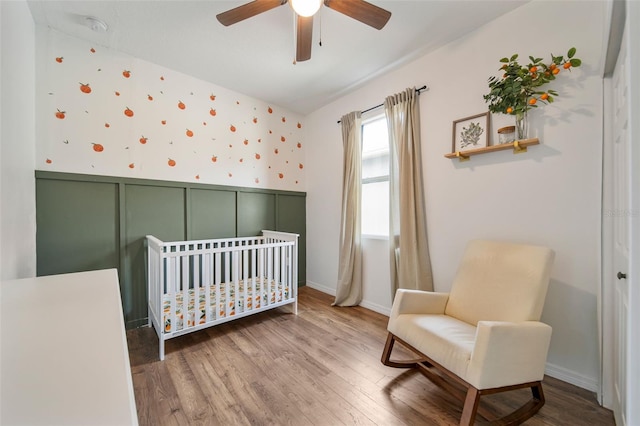 bedroom featuring a crib, wallpapered walls, wainscoting, wood finished floors, and a decorative wall