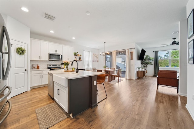 kitchen featuring stainless steel appliances, an island with sink, light countertops, and white cabinetry