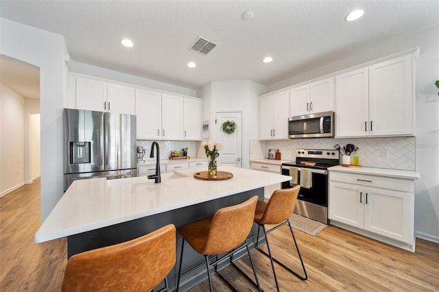 kitchen featuring stainless steel appliances, light countertops, visible vents, white cabinets, and a kitchen island with sink