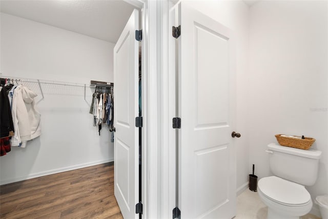 bathroom with a spacious closet, wood finished floors, toilet, and baseboards