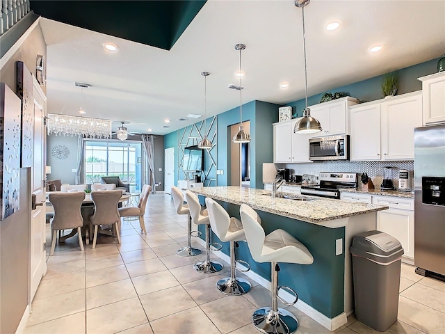 kitchen featuring pendant lighting, stainless steel appliances, light stone counters, white cabinets, and a center island with sink