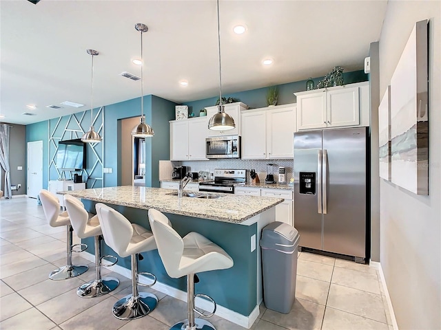 kitchen featuring stainless steel appliances, hanging light fixtures, a center island with sink, and white cabinets