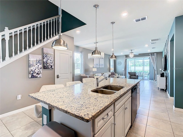 kitchen with sink, a breakfast bar area, light stone countertops, an island with sink, and light tile patterned flooring