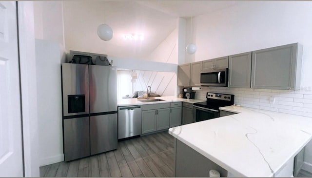 kitchen featuring a peninsula, stainless steel appliances, light countertops, pendant lighting, and a sink