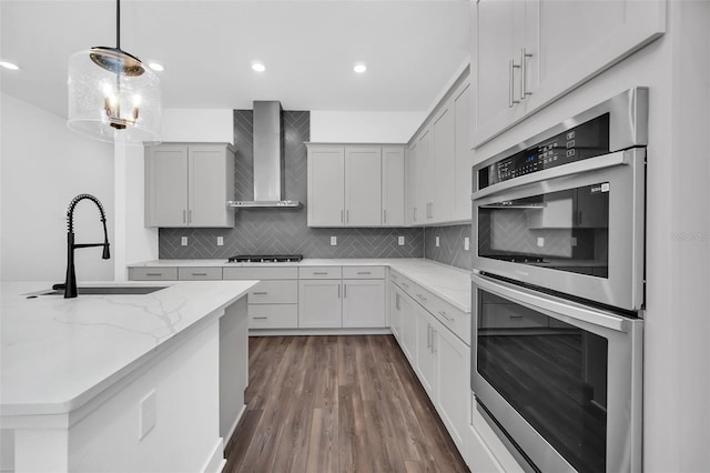 kitchen featuring sink, light stone counters, decorative light fixtures, stainless steel appliances, and wall chimney range hood