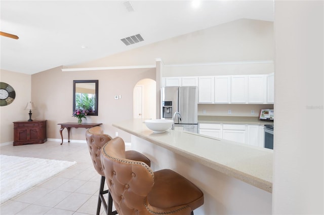 kitchen featuring lofted ceiling, light tile patterned floors, a kitchen breakfast bar, stainless steel appliances, and white cabinets