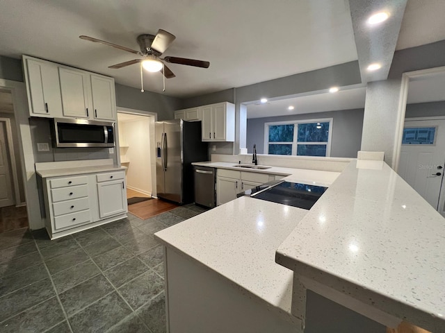 kitchen with sink, appliances with stainless steel finishes, light stone counters, white cabinets, and kitchen peninsula