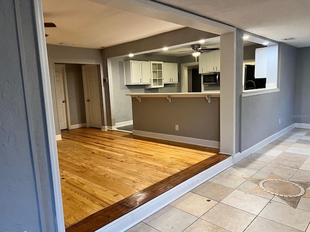 kitchen featuring ceiling fan, kitchen peninsula, white cabinets, and light tile patterned flooring