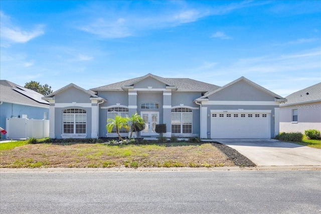 view of front of property with french doors, stucco siding, concrete driveway, an attached garage, and fence