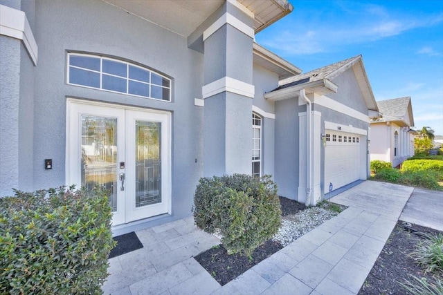 view of exterior entry with driveway, an attached garage, and stucco siding