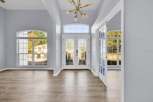 foyer entrance featuring arched walkways, a notable chandelier, wood finished floors, baseboards, and french doors