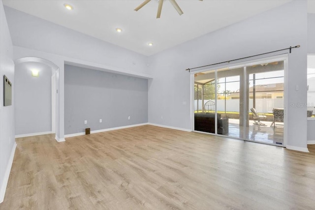 unfurnished living room featuring arched walkways, recessed lighting, light wood-style flooring, a ceiling fan, and baseboards