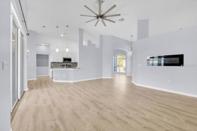 unfurnished living room featuring visible vents, arched walkways, a towering ceiling, ceiling fan, and light wood-style flooring