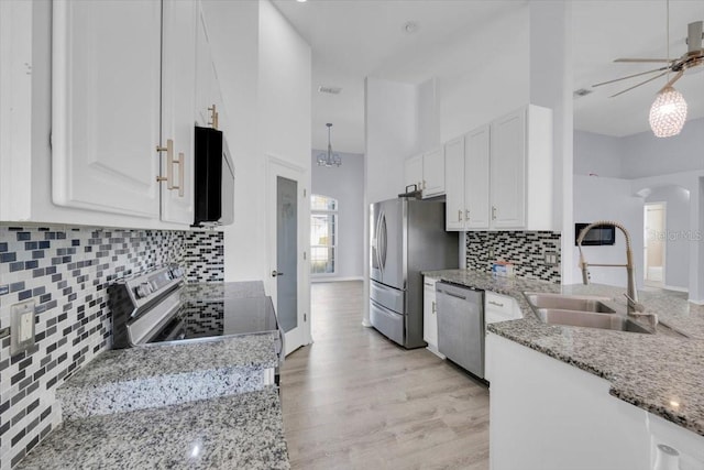 kitchen with arched walkways, light stone counters, appliances with stainless steel finishes, white cabinetry, and a sink