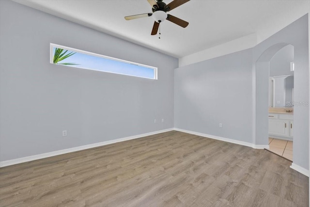 unfurnished bedroom featuring baseboards, arched walkways, ceiling fan, ensuite bathroom, and light wood-type flooring