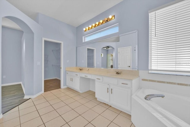 bathroom featuring a walk in closet, double vanity, tile patterned floors, baseboards, and a bath