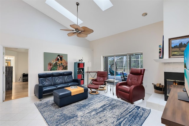 living room featuring light tile patterned flooring, a skylight, a tiled fireplace, ceiling fan, and high vaulted ceiling
