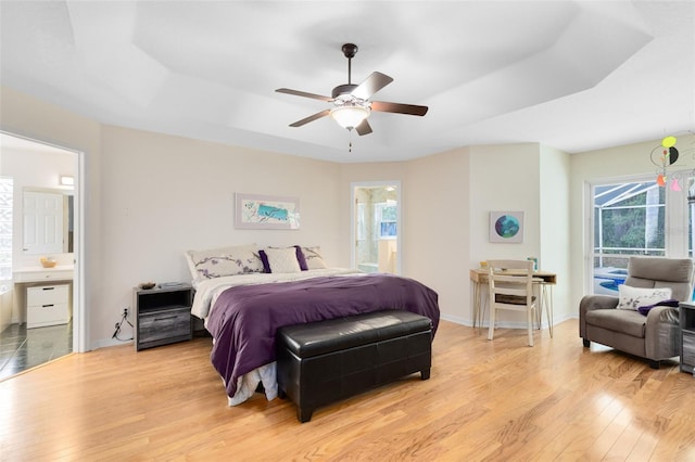 bedroom featuring light hardwood / wood-style flooring, access to outside, connected bathroom, and a raised ceiling