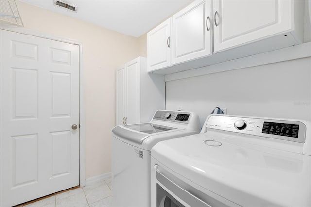 clothes washing area with cabinets, washing machine and dryer, and light tile patterned floors