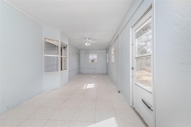 hallway featuring light tile patterned floors, a textured wall, and plenty of natural light