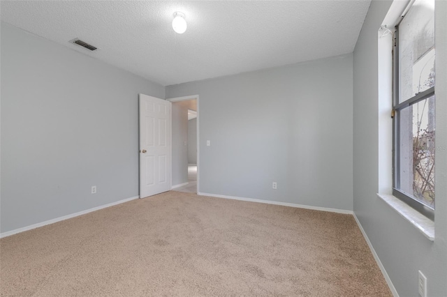 carpeted empty room with baseboards, visible vents, and a textured ceiling